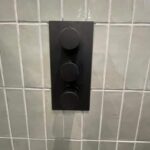 a black rectangular object with knobs on a tile wall